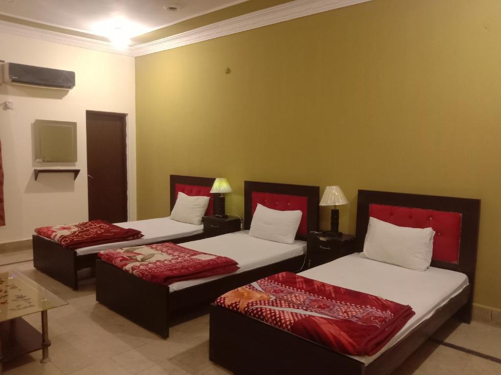 Zimmer mit 3 Betten mit roter und weißer Bettwäsche in der Unterkunft Regal Guest House in Bahawalpur