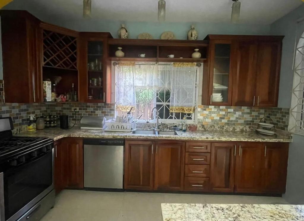 a kitchen with wooden cabinets and a sink and a window at Cozy Elegance 3 Bedroom Estate in Portmore