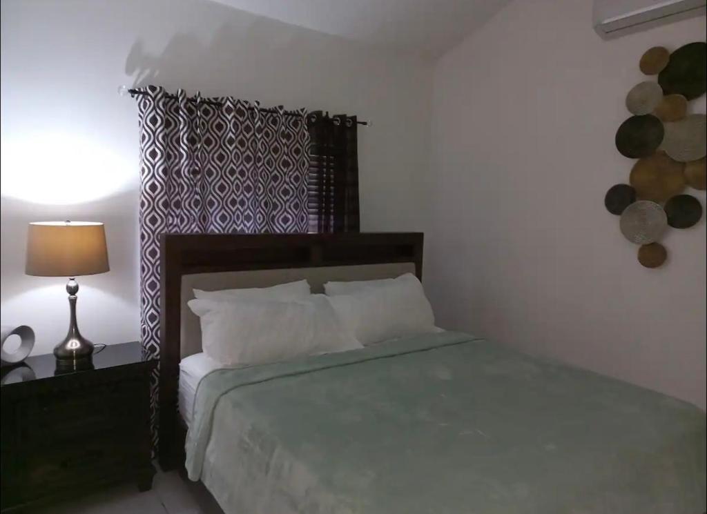 a bedroom with a bed and a table with a lamp at Mi Casa Comfort Estate in Portmore
