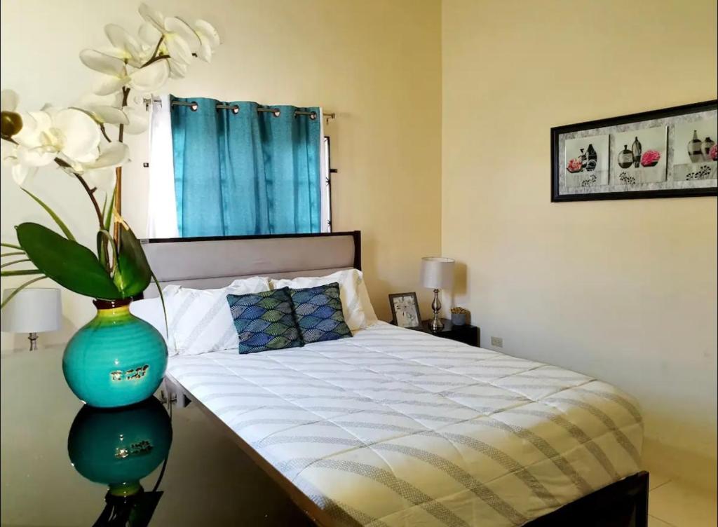 - une chambre dotée d'un lit avec un vase bleu et une fleur dans l'établissement Gems Pool Side Chillax Stay, à Portmore