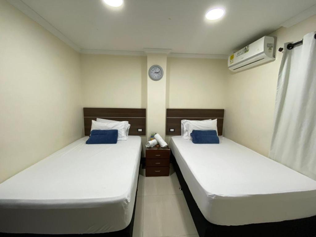two twin beds in a room with a clock on the wall at Hotel santa fe plaza sucursal HBP in Santa Fe de Antioquia