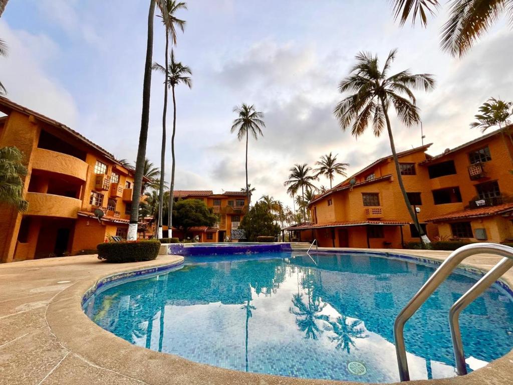 une grande piscine avec des palmiers et des bâtiments dans l'établissement Un Oasis entre Olas y Palmeras con Playa Privada, à Tucacas