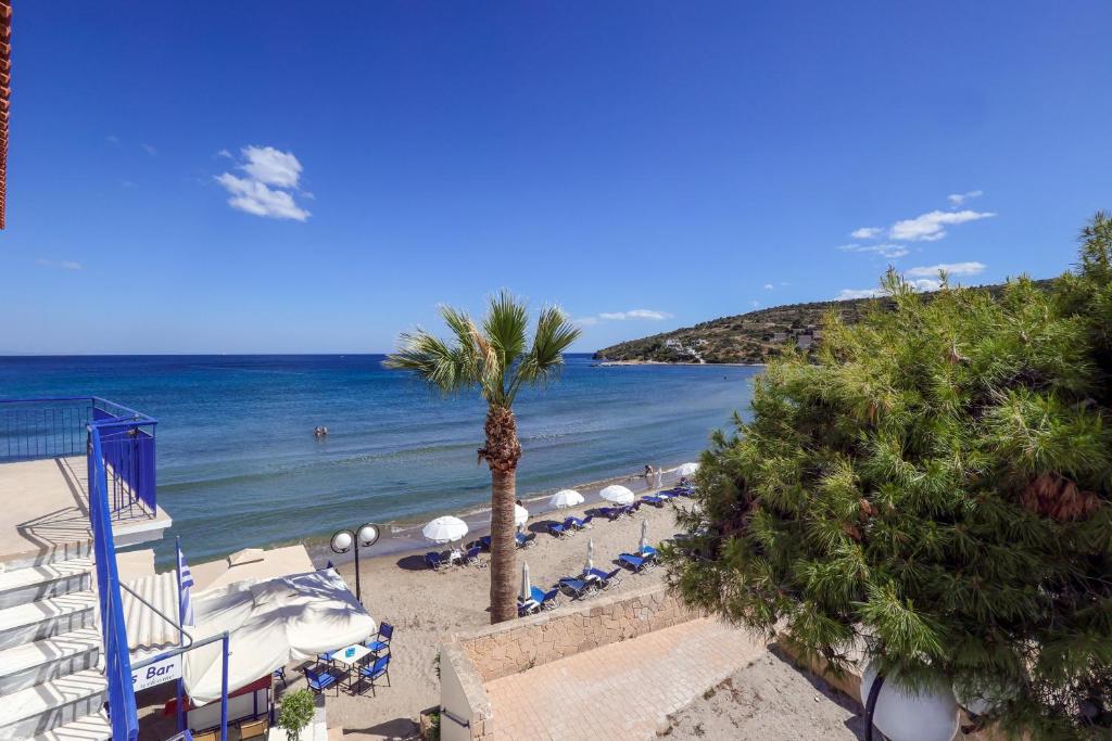 a beach with chairs and a palm tree and the ocean at Niko's Beach Suites ΔΥΟ in Agia Marina Aegina