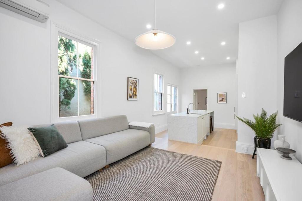 sala de estar blanca con sofá y cocina en Cozy North Melbourne Family Retreat, en Melbourne