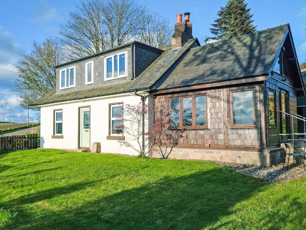 une maison blanche avec un toit noir sur une pelouse verte dans l'établissement Greve Cottage, à Marykirk