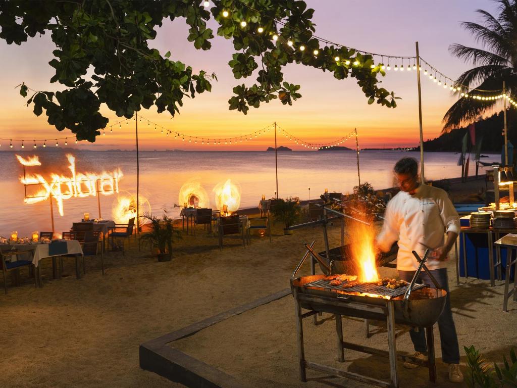 a man cooking food on a grill on the beach at Explorar Koh Phangan - Adults Only Resort and Spa in Haad Rin