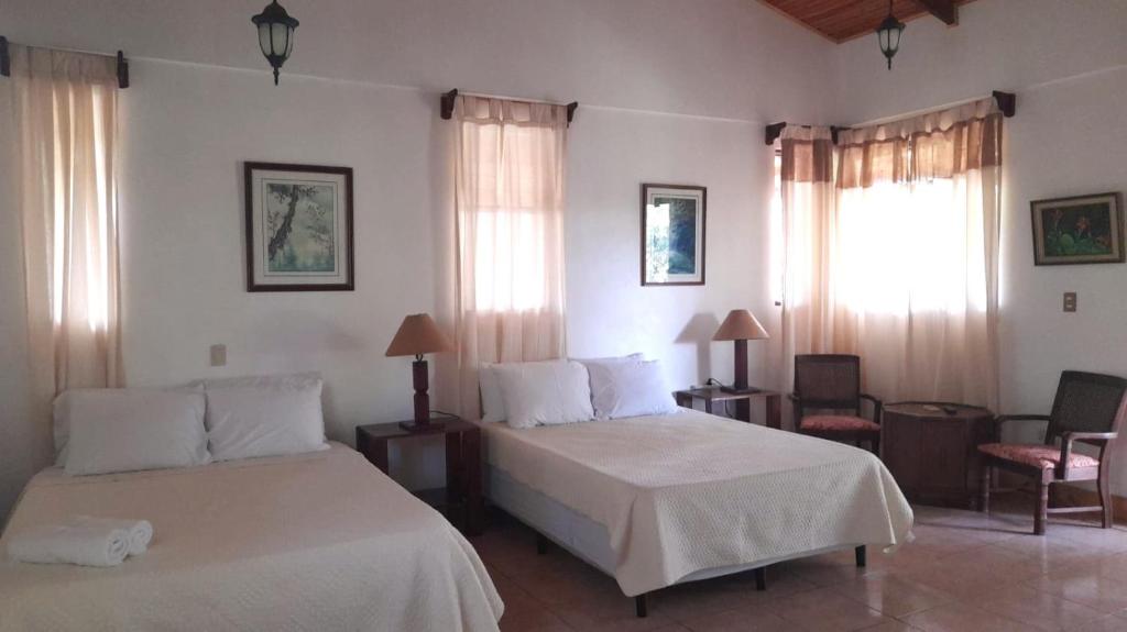 1 dormitorio con 2 camas, silla y ventanas en Hotel Cacao Río Celeste, en Bijagua