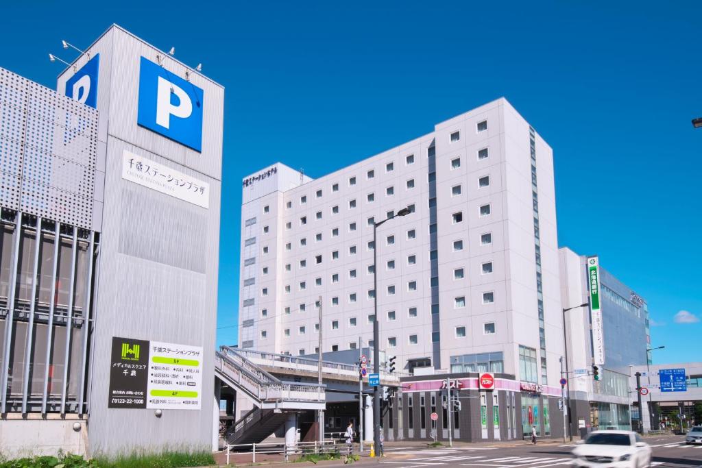 a large white building with a parking sign next to a street at Chitose Station Hotel in Chitose