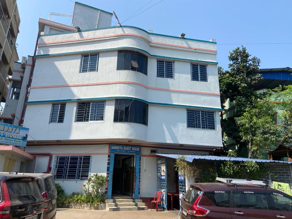 a white building with a red car parked in front of it at Sandhya Guest House in Digha