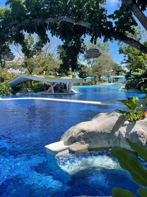 a swimming pool with blue water and a tree at Ma Roberta - Tambuli Resort with fast Wifi 16 Floor Studio Type in Lapu Lapu City