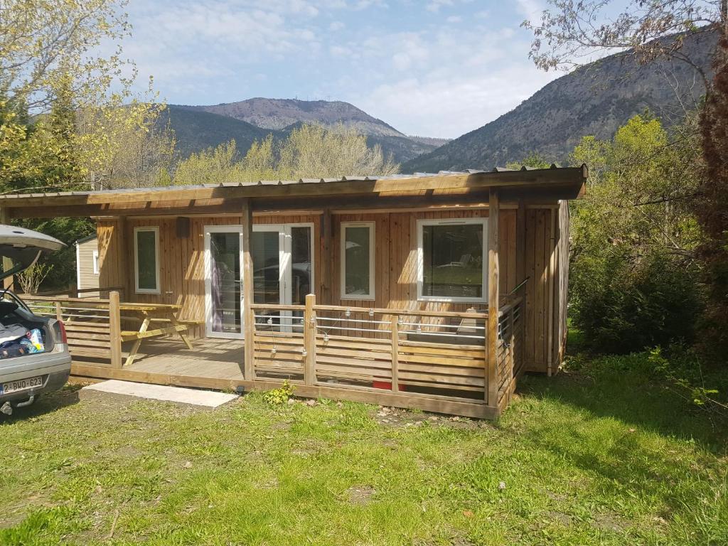 une cabane en bois avec une terrasse couverte et des montagnes en arrière-plan dans l'établissement Mobilhome Serre Ponçon, à Rochebrune