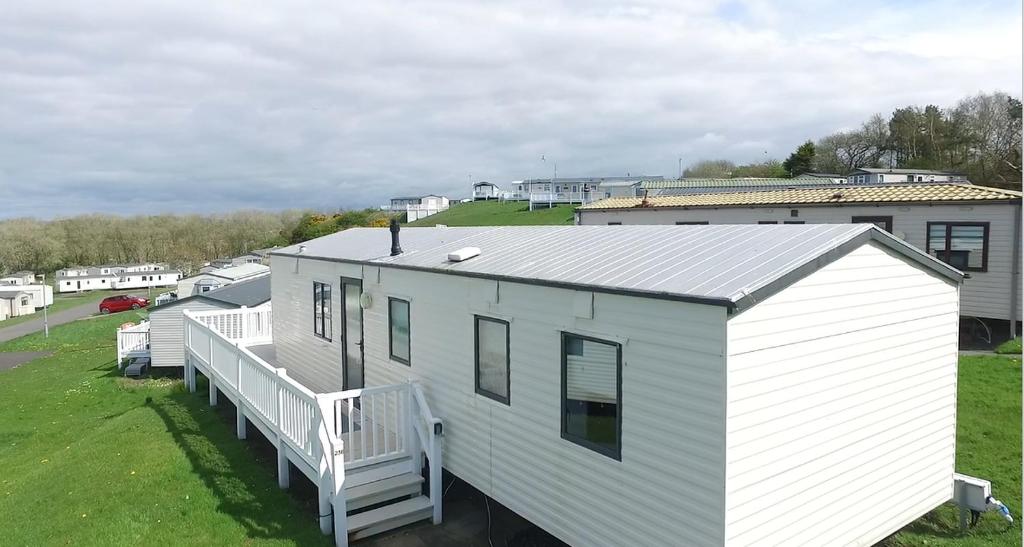 a white house with a porch and a yard at 238 Arran View, Craig Tara Holiday Park in Ayr