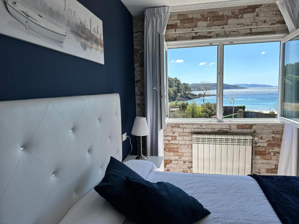 a bedroom with a white bed and a large window at Hotel Playa de Sardiñeiro in Finisterre