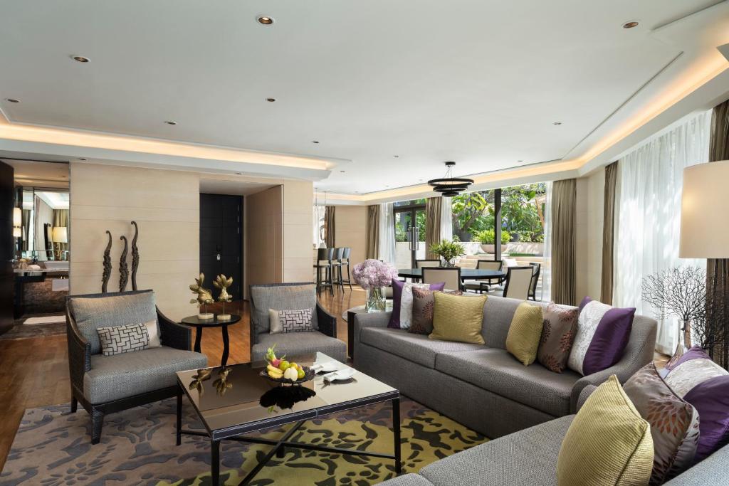 A colorful contemporary living room with a deep sofa, patterned rug, armchairs, and greenery beyond the windows.