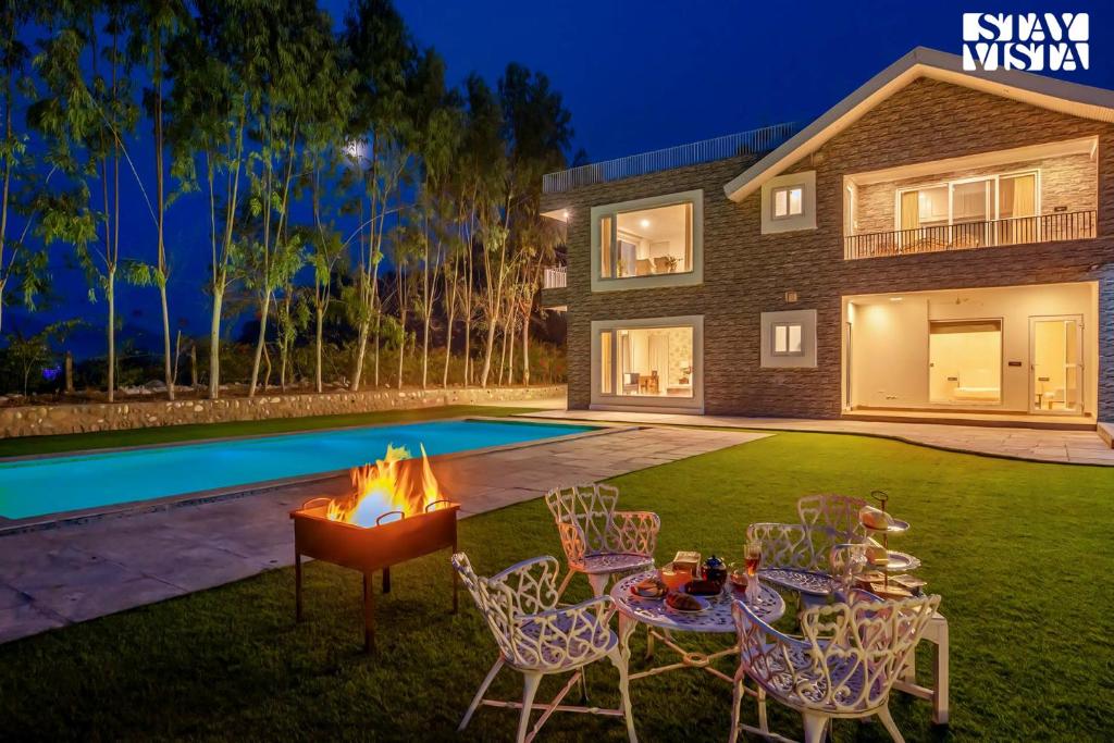 昌迪加爾的住宿－StayVista's Silver Slopes - Mountain-View Villa with Outdoor Pool, Expansive Lawn featuring a Gazebo & Terrace，后院设有火坑、椅子和游泳池