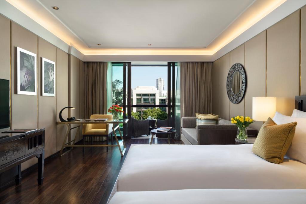 A large bedroom includes a king bed, window-side seating, a desk, and a partial city view.