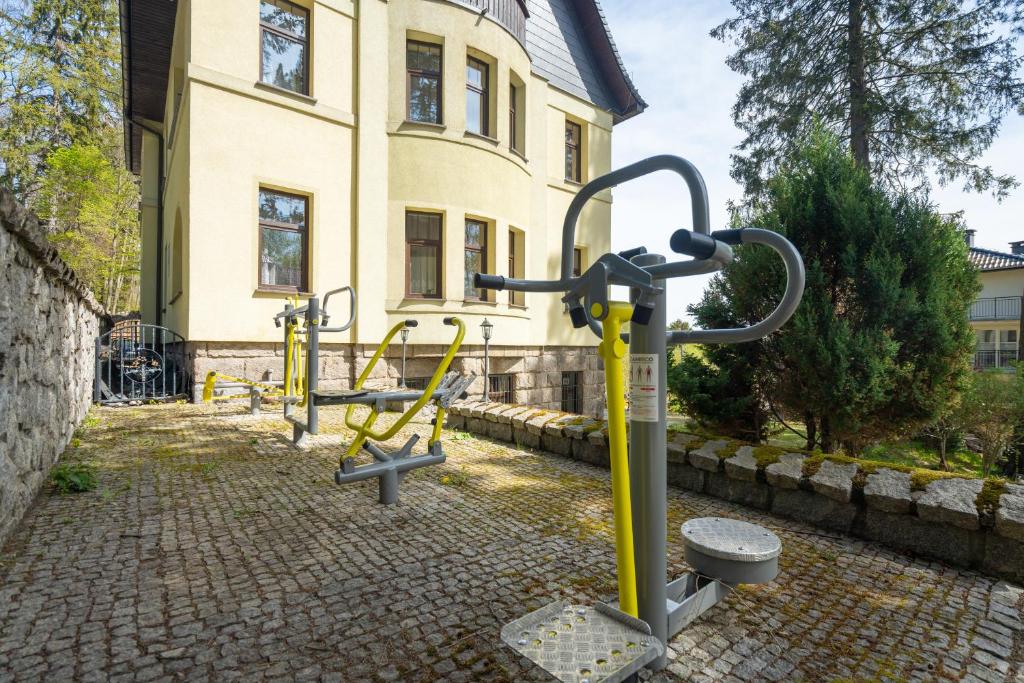 Outdoor fitness equipment installed on cobblestone patio beside a pale villa, surrounded by trees.