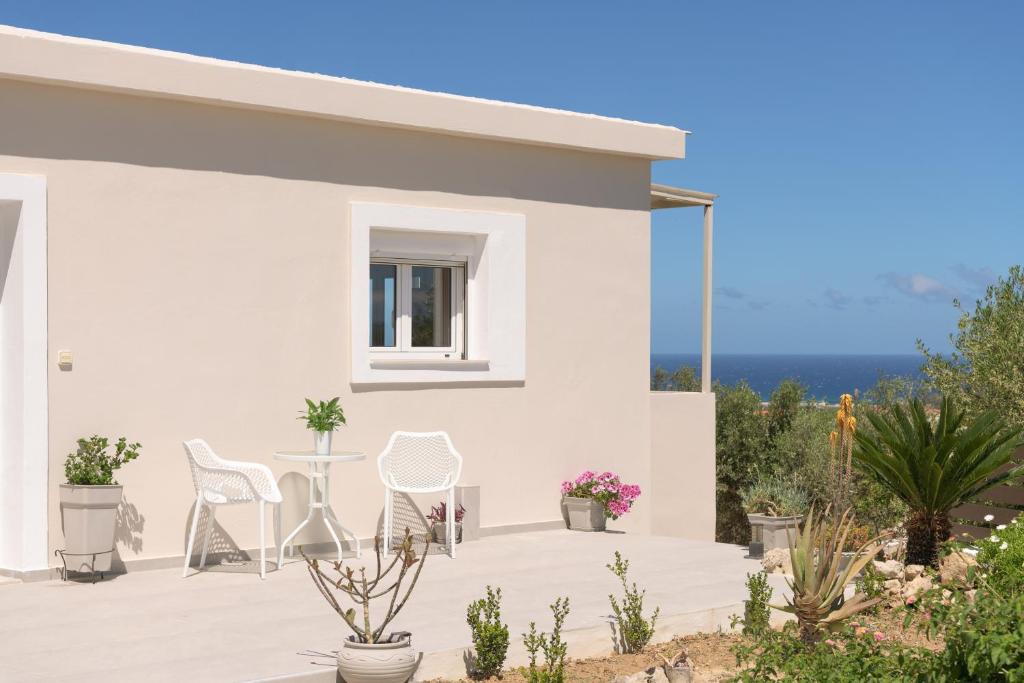 Ein weißes Haus mit einer Terrasse mit Stühlen und einem Tisch in der Unterkunft Perivoli Cottage, a Rural Bliss of Nature, By ThinkVilla in Agios Dimitrios