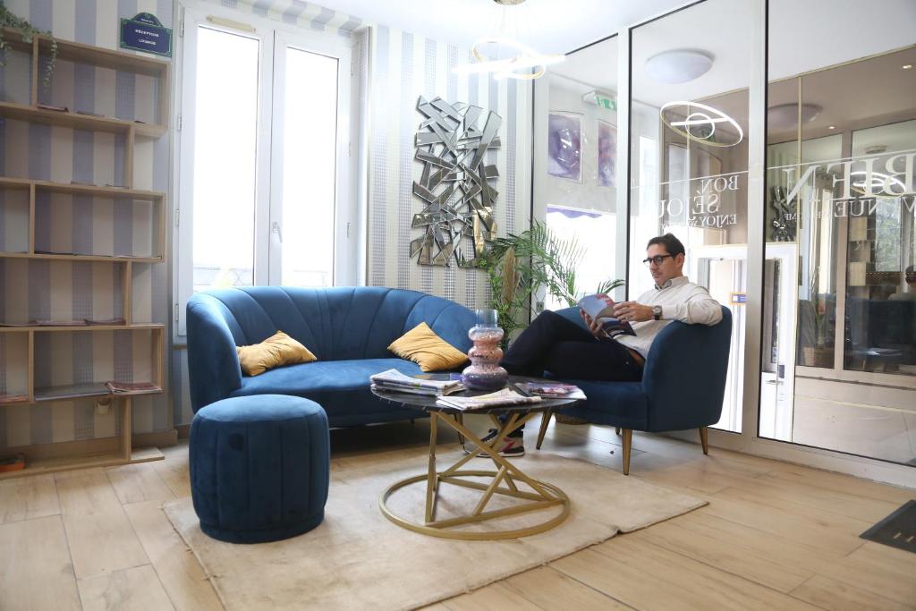 un hombre sentado en una silla azul en una sala de estar en Hotel Arc Paris Porte d&#39;Orléans, en Montrouge