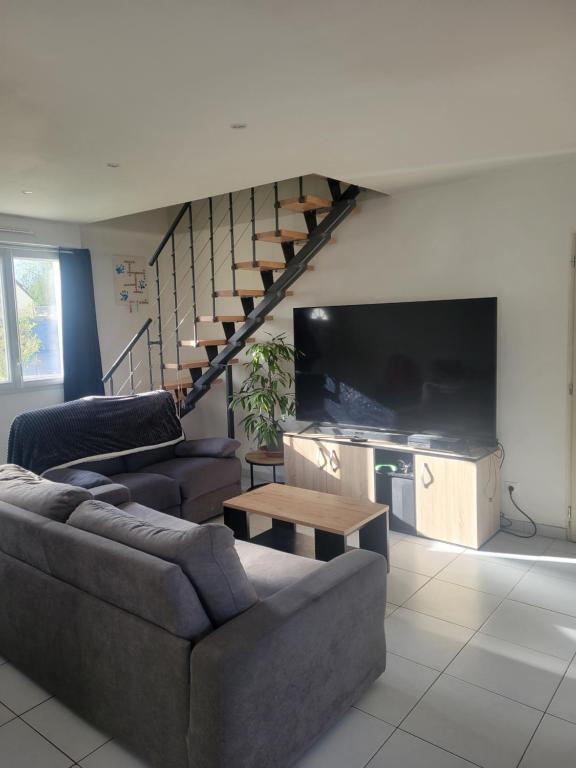 a living room with a couch and a tv and a staircase at Chambre d'hôtes Goustranville in Goustranville