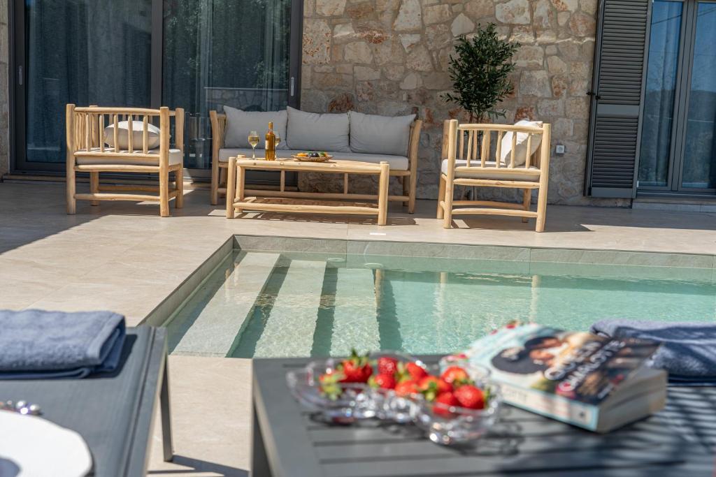 einen Pool mit zwei Stühlen und einem Tisch mit Obst darauf in der Unterkunft F&A Golden Stone Villa in Loukáta