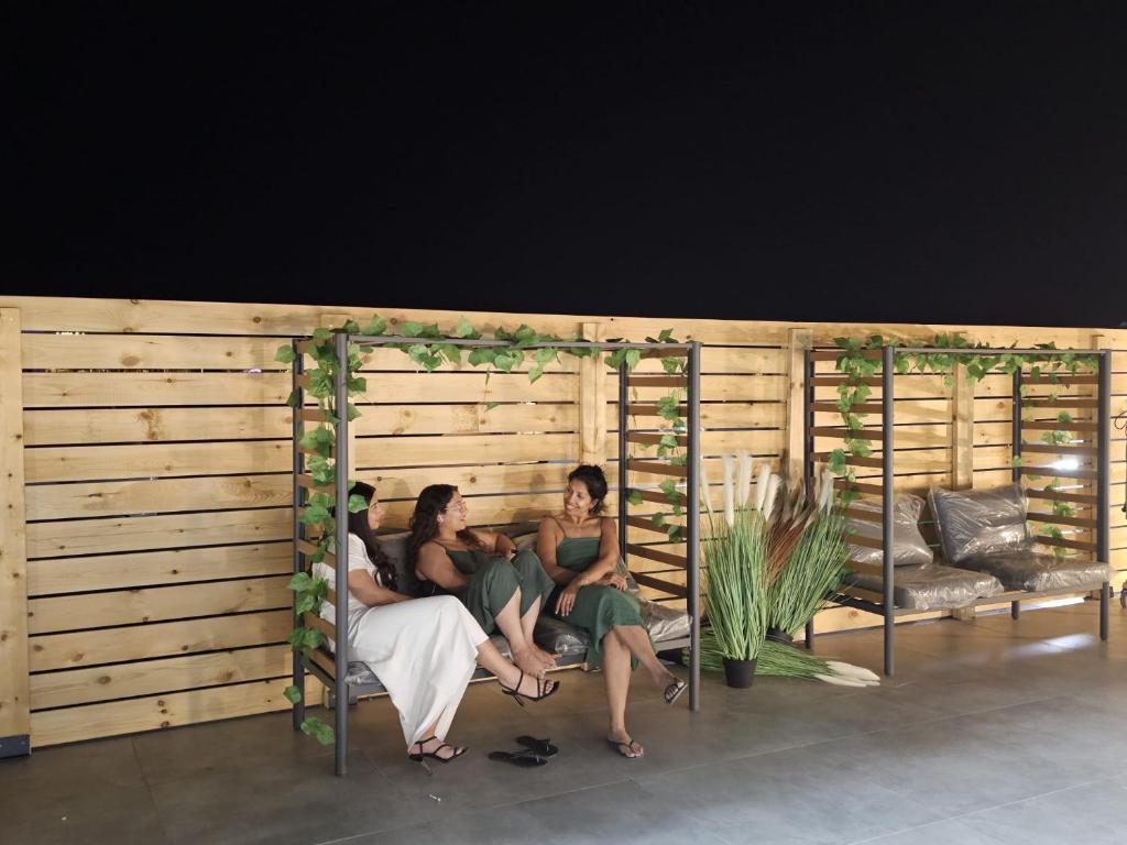 drei Frauen sitzen auf einer Bank in einer Holzwand in der Unterkunft Sun Sea Center in Eilat