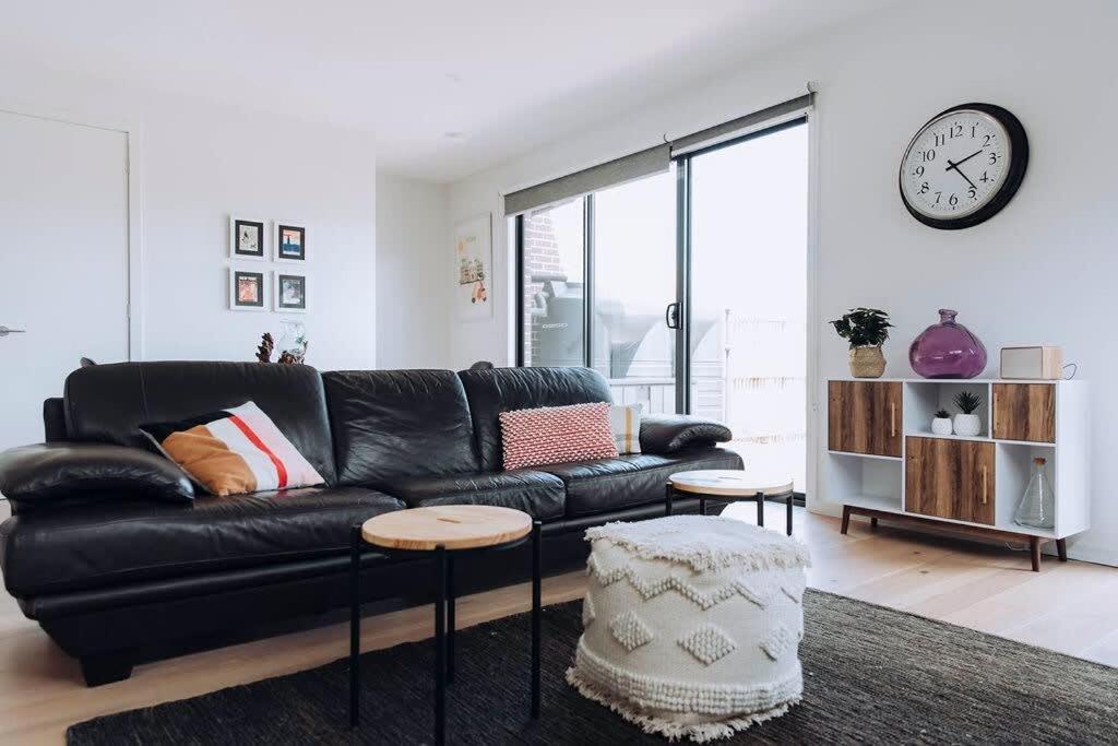 a black leather couch in a living room with a clock at MODERN LUXE TOWNHOUSE / ROSEBUD in Rosebud