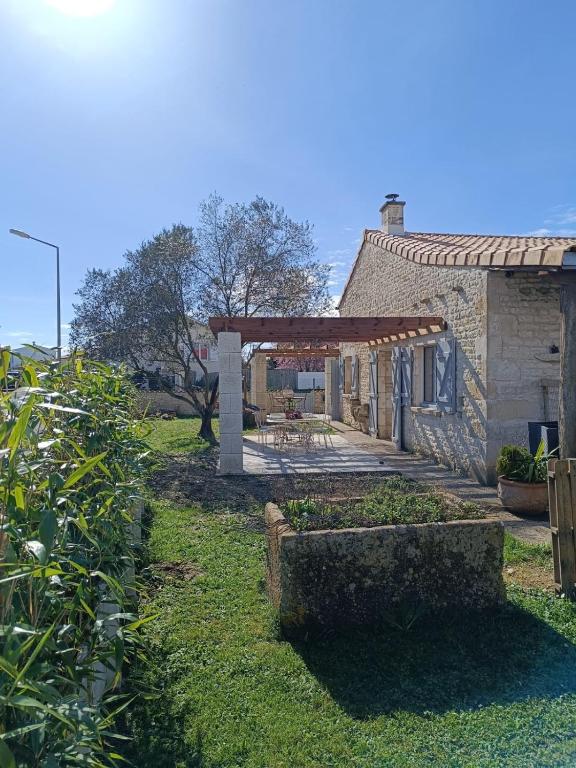un jardin avec un bâtiment en pierre avec une pergola en bois dans l'établissement Studio 20 m2 avec salle d'eau et cuisine privatives, à Aigrefeuille-dʼAunis