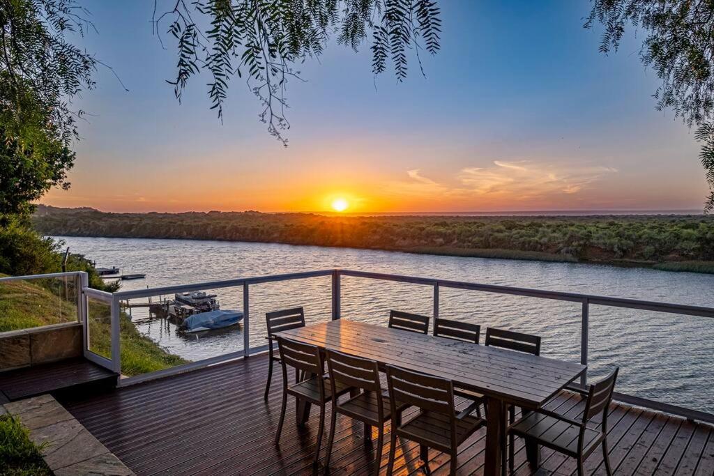 a wooden deck with a table and chairs and a sunset at The River House - Addo Elephant in Gqeberha