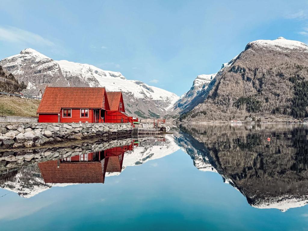 a red house on the side of a lake with snow covered mountains at Holiday Home Elghytta - FJS006 by Interhome in Balestrand