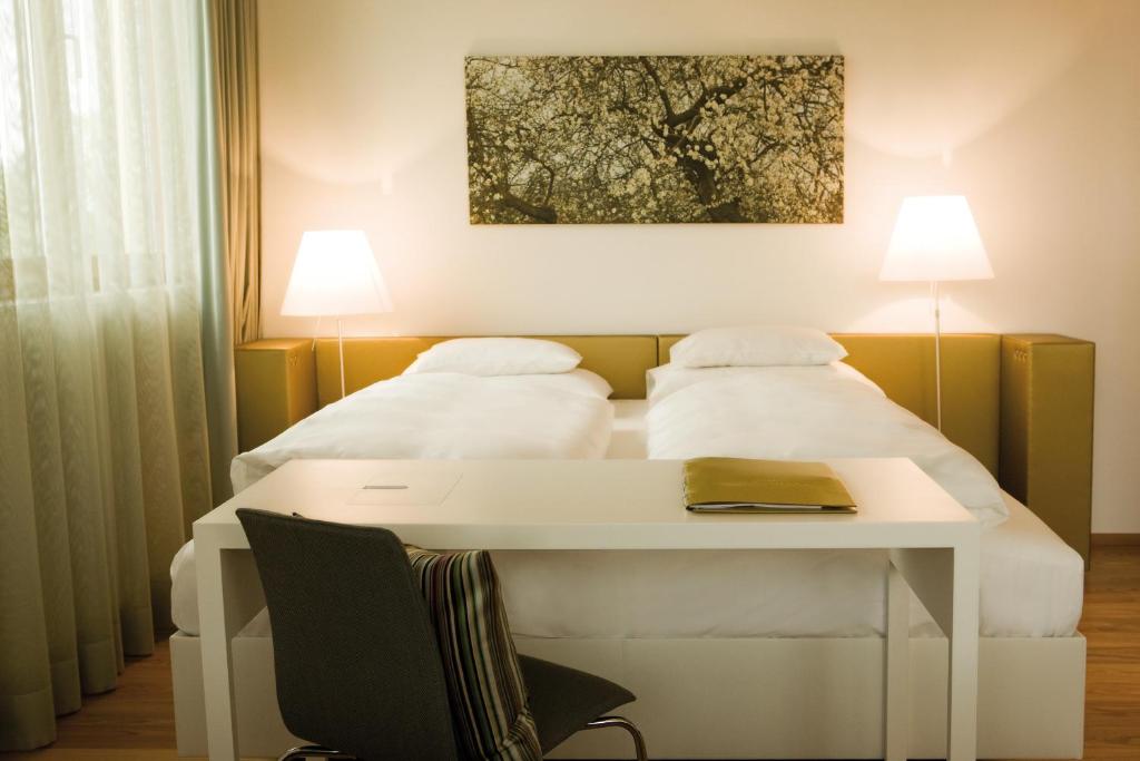 a bedroom with a bed with a table and two pillows at Hotel am See in Hard