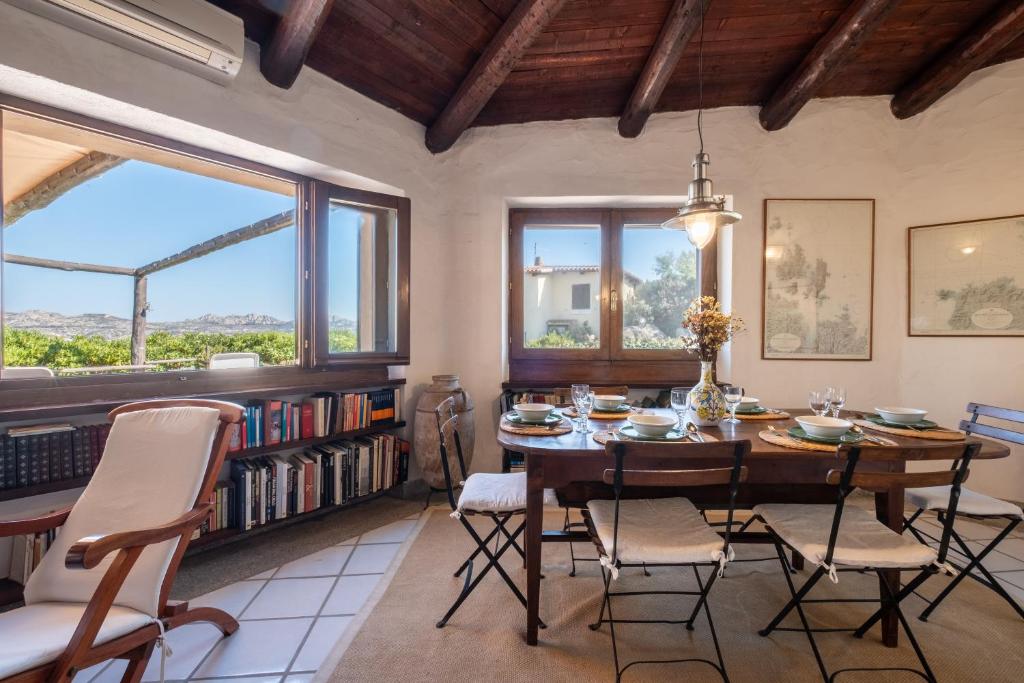 una sala da pranzo con tavolo, sedie e finestre di Discesa a Mare-Villa Esclusiva Vista Caprera a Casale Azara