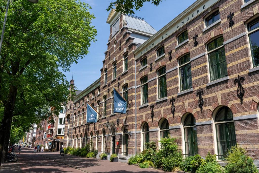 阿姆斯特丹的住宿－YAYS Amsterdam Maritime by Numa，砖砌的建筑,上面有两面蓝旗