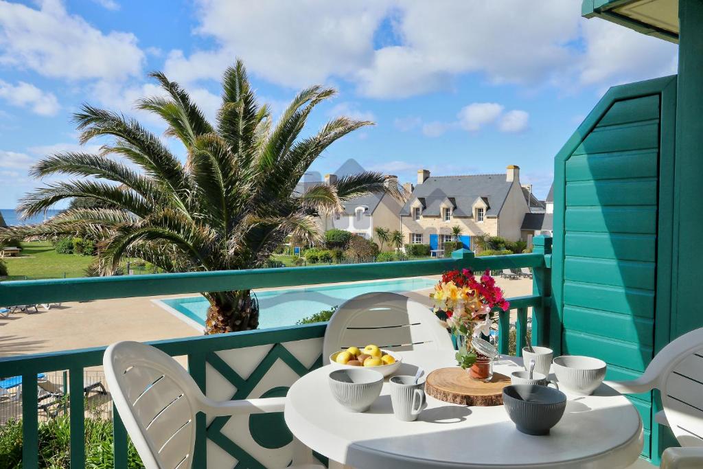 a table on a balcony with a view of the ocean at LocaLise - A18 - Appartement avec balcon - Petite vue mer à travers le palmier - Piscine de avril à septembre - Wifi inclus - Animaux admis - Draps inclus - Parking inclus in Le Guilvinec