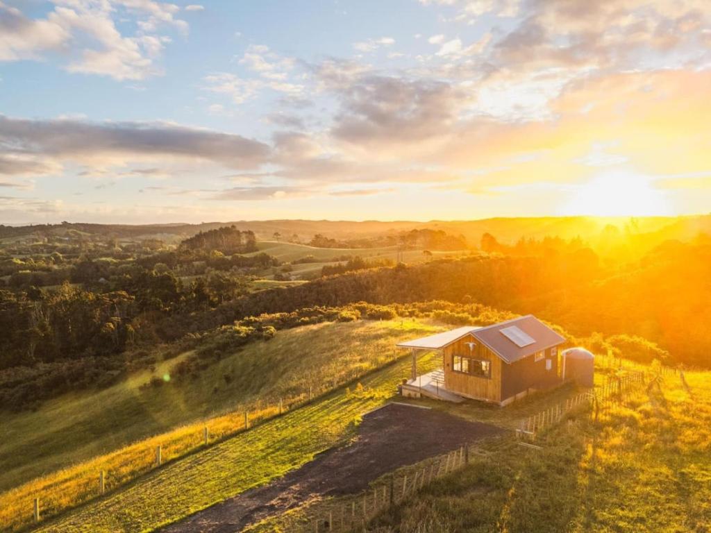 a small house on a hill with the sun in the background at Romantic hilltop hideaway - Skyview Cottage in Dairy Flat