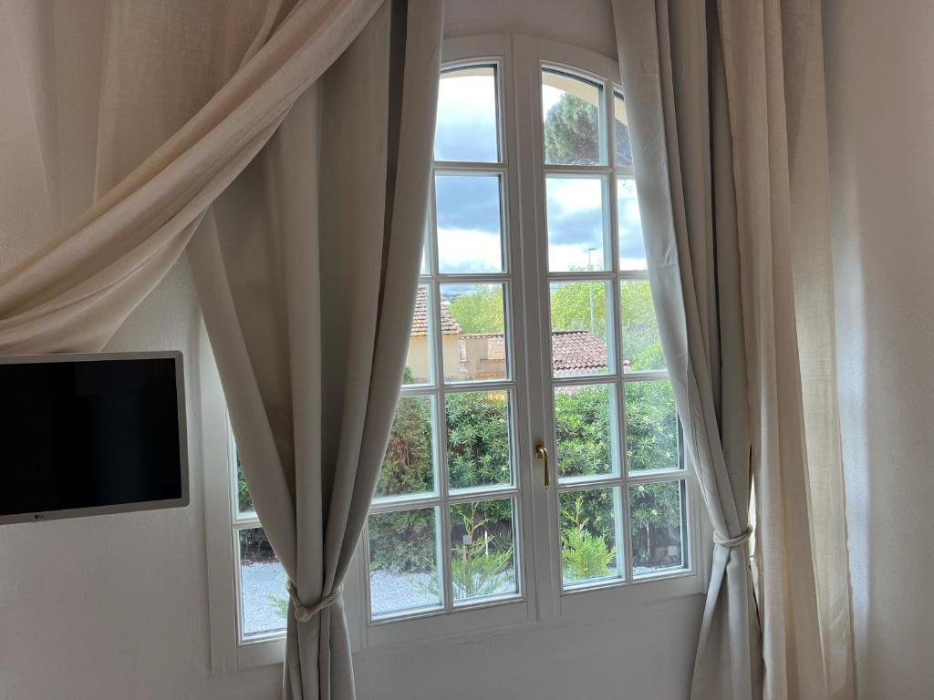 a room with a window with curtains and a television at Maison d'Orange - La Pinede in Saint-Tropez