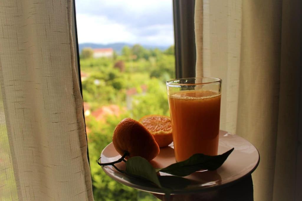 a glass of orange juice on a plate next to a window at Miguas House in Baião