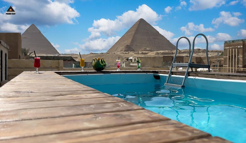 a swimming pool with pyramids in the background at Pyramids Height Hotel & Pyramids Master Scene Rooftop in Cairo