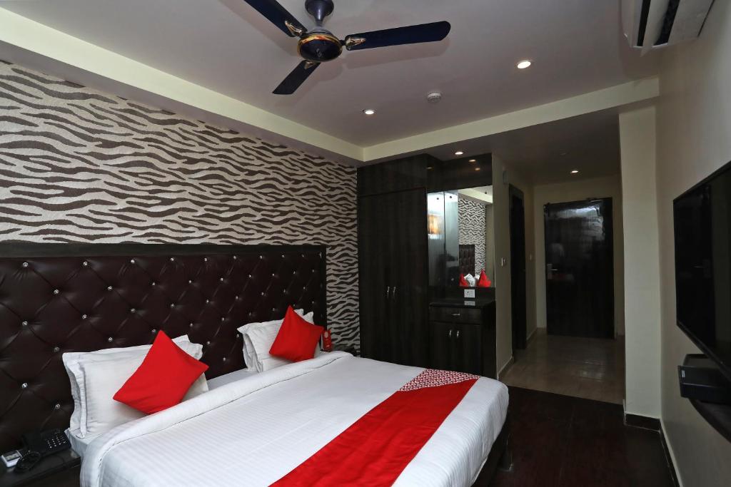 OYO Hotel Maan في جورجاون: غرفة نوم مع سرير مع وسائد حمراء ومروحة سقف
