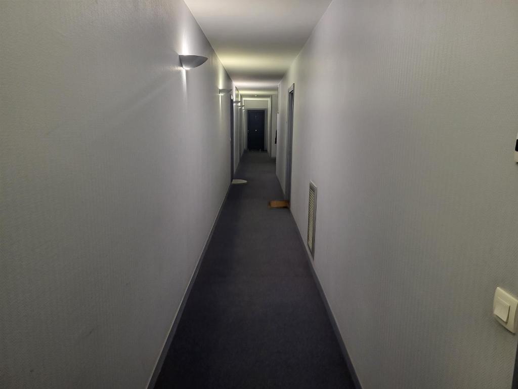 un long couloir avec des murs blancs et un grand sol noir dans l'établissement Aibnb Paris Stade de France notre-Dame Tour Eiffel, à Saint-Denis