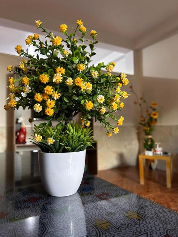プカルパにあるALAMEDAS APARMENTsのテーブルの上に黄色い花が咲き誇る白い花瓶
