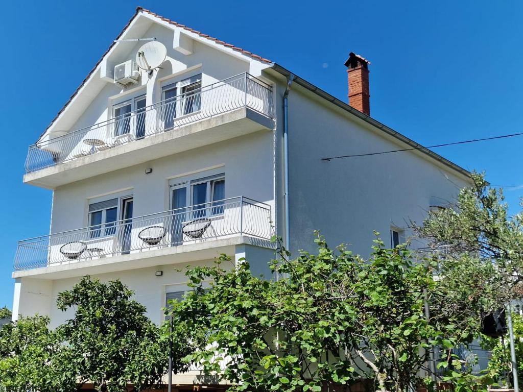 a white apartment building with a balcony and trees at Apartmani Zinda in Sukošan