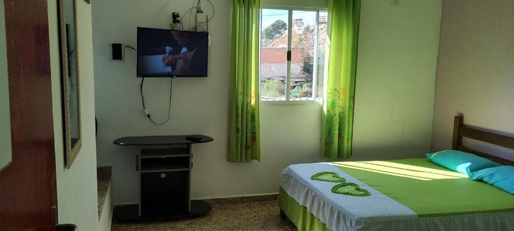 1 dormitorio con 1 cama con cortinas verdes y TV en Kit net montanha mágica en São Thomé das Letras