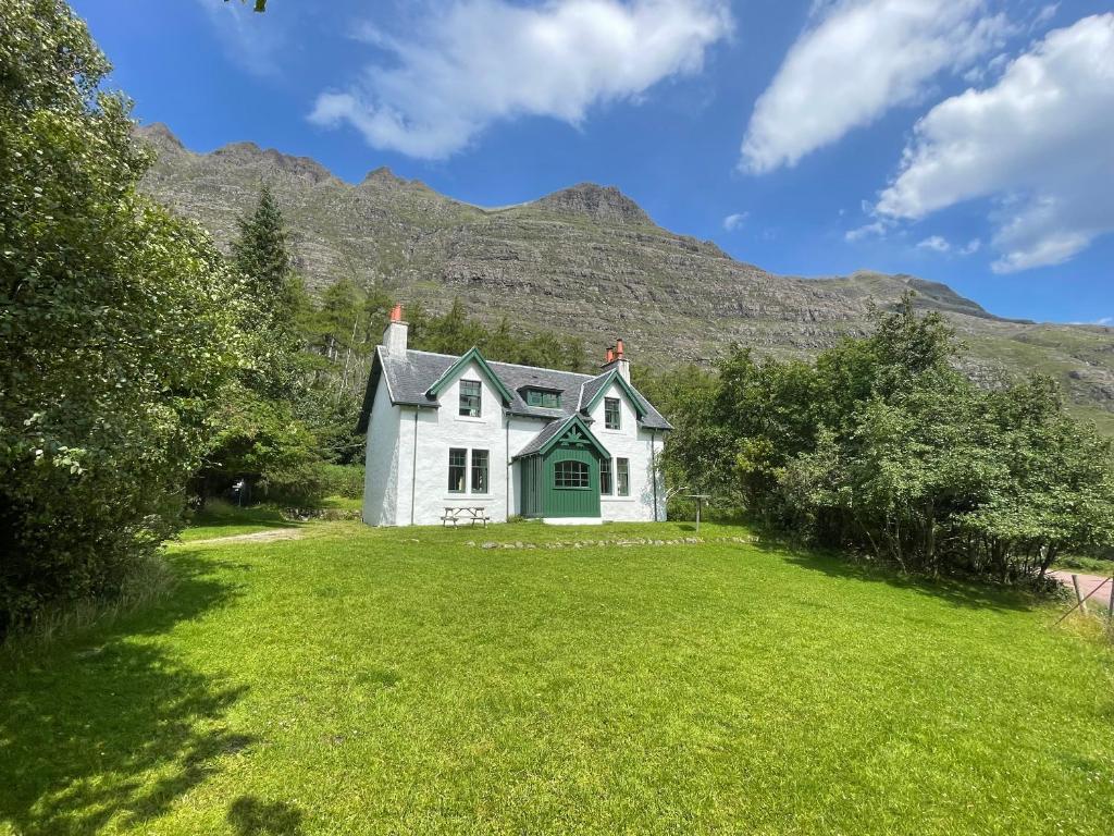 a white house in a field with mountains in the background at Glen Cottage - Torridon in Achnasheen