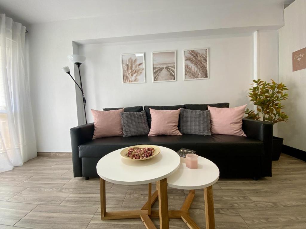 Apartamento Beli Málaga في بينالمادينا: غرفة معيشة مع أريكة سوداء وطاولتين