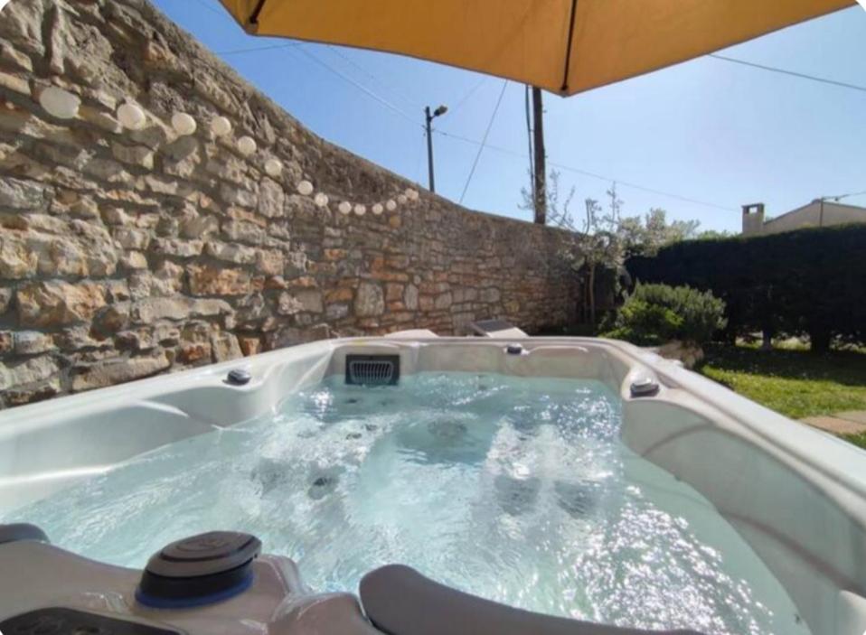 a hot tub in a stone wall with an umbrella at Apartment with Whirlpool and BBQ near Poreč in Baderna