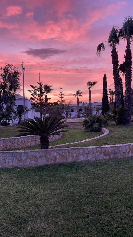una puesta de sol en un parque con palmeras y una pared de piedra en Villa Angela case vacanza, en Vieste