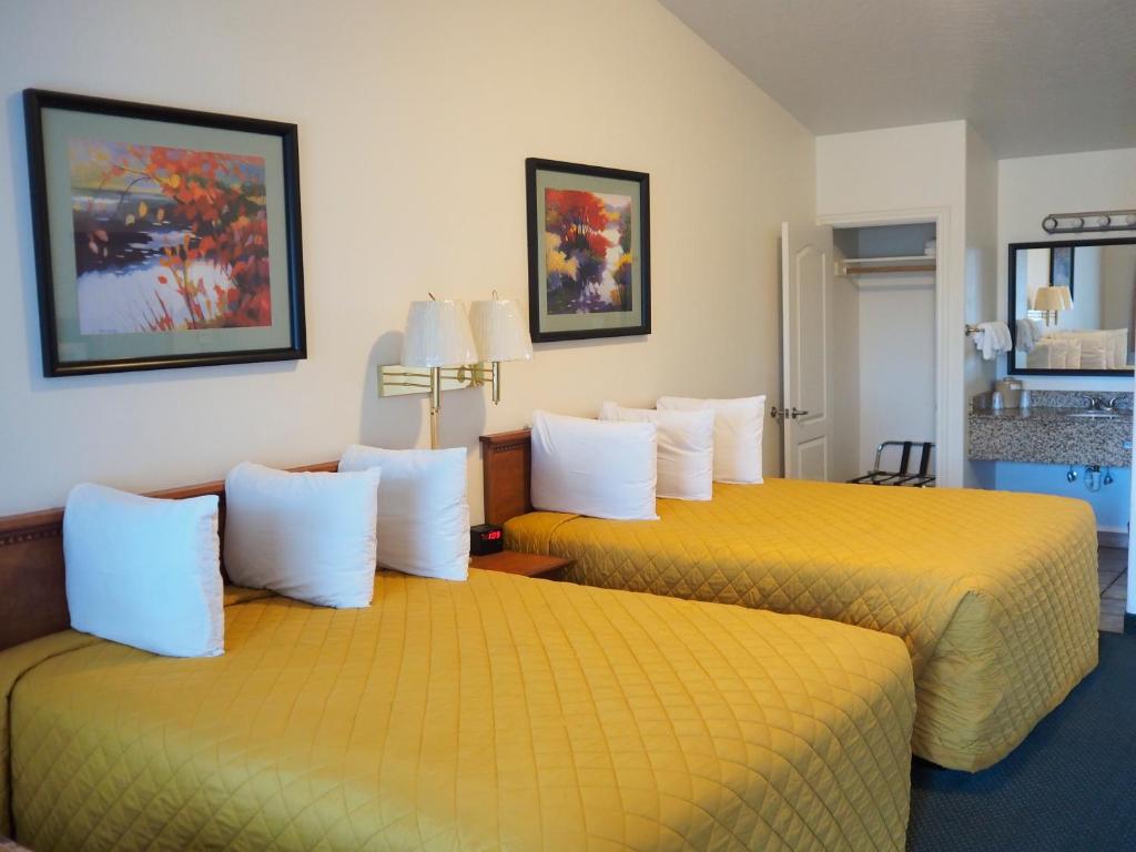 2 Betten in einem Hotelzimmer mit gelber Bettwäsche in der Unterkunft Wild Rivers Motorlodge in Brookings