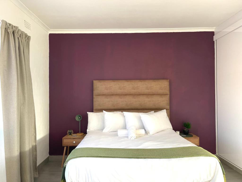 een slaapkamer met een groot bed met een paarse muur bij Pristine Guest Apartments in Mthatha