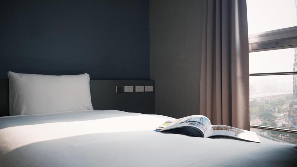 a bed with a book on it next to a window at Hotel Leisure 台中輕行旅 in Taichung